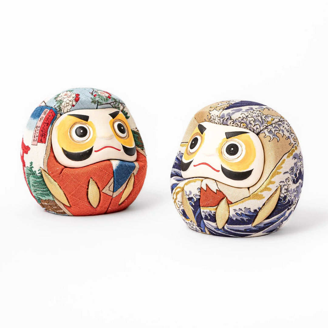 Two fabric daruma ornaments with multicolor kimono patterns displayed on wooden stands side by side