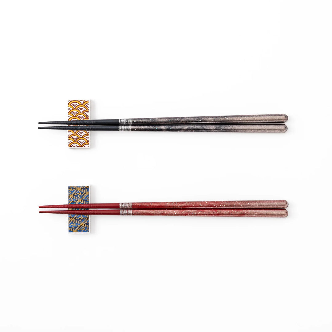 A pair of black and red lacquer Japanese chopsticks with two rectangular ceramic chopstick rests featuring traditional patterns