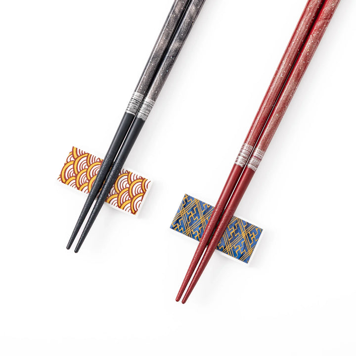 A pair of black and red lacquer Japanese chopsticks with two rectangular ceramic chopstick rests featuring traditional patterns