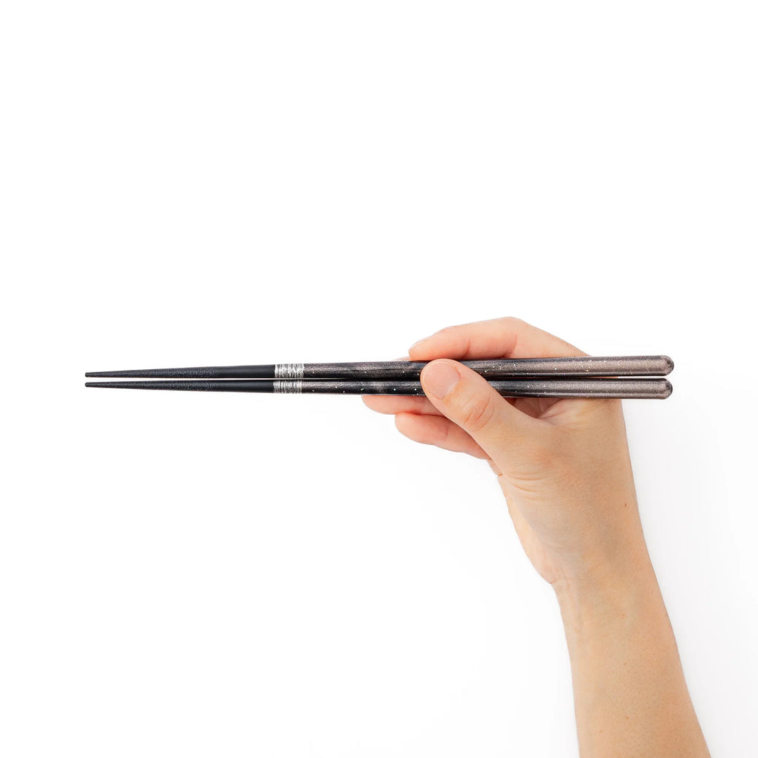 A hand holding a pair of black sparkling Japanese lacquer chopsticks to demonstrate a comfortable grip and standard length