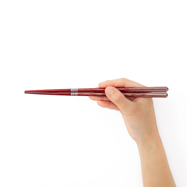 A hand holding a pair of red sparkling Japanese lacquer chopsticks showcasing the elegant glitter gradient finish