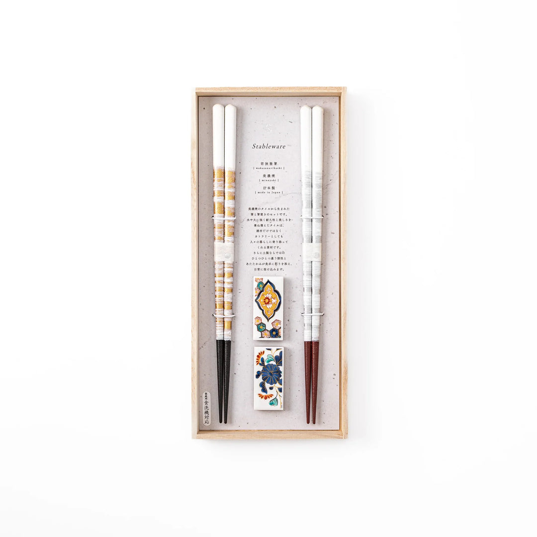 A pair of gold and silver textured Japanese chopsticks with two rectangular ceramic chopstick rests featuring floral patterns