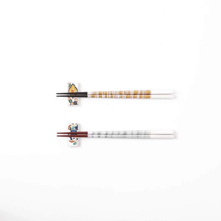 A pair of gold and silver textured Japanese chopsticks with two rectangular ceramic chopstick rests featuring floral patterns