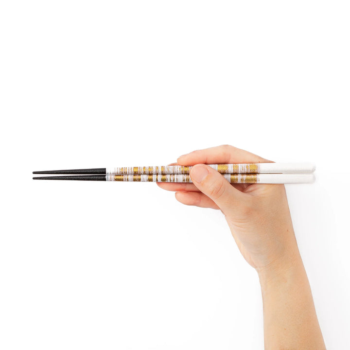 A hand holding a pair of gold textured Japanese chopsticks to demonstrate a comfortable natural grip and standard length