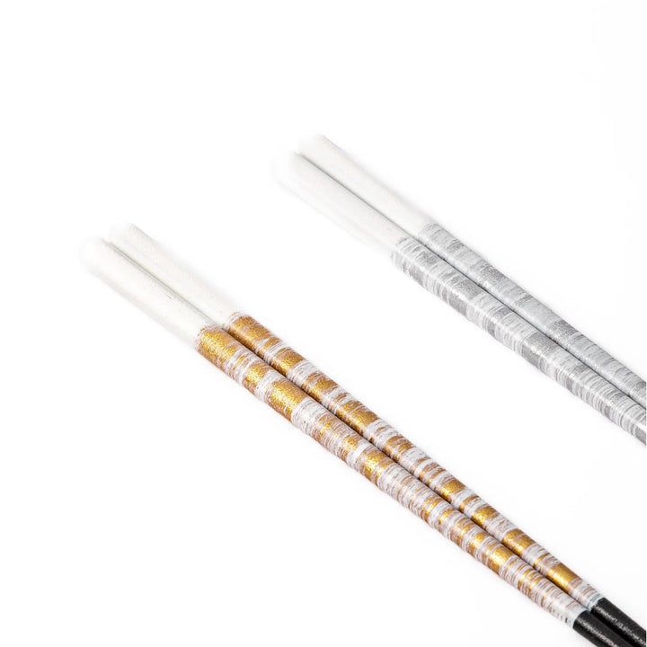 Close up of gold and silver Japanese chopsticks showing a beautiful textured metallic foil finish on a white background