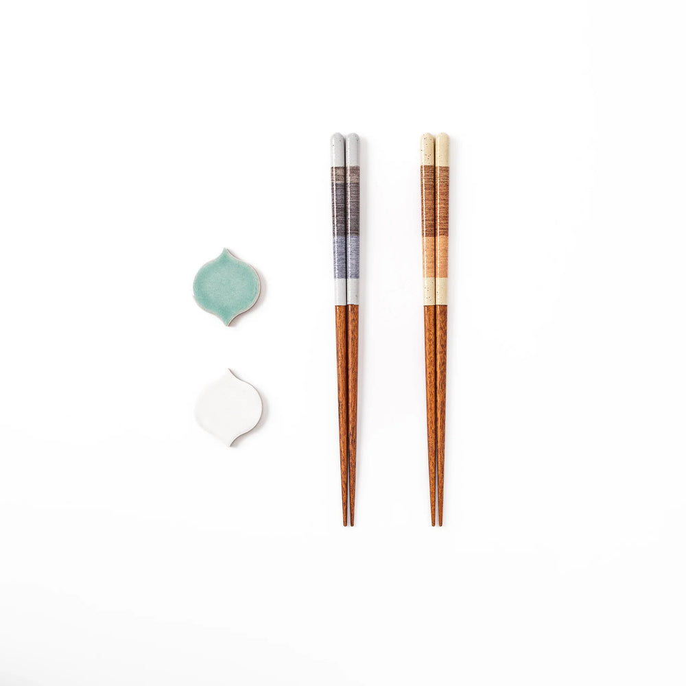 Two pairs of natural wood Japanese chopsticks resting on blue and white curved tile style ceramic chopstick rests