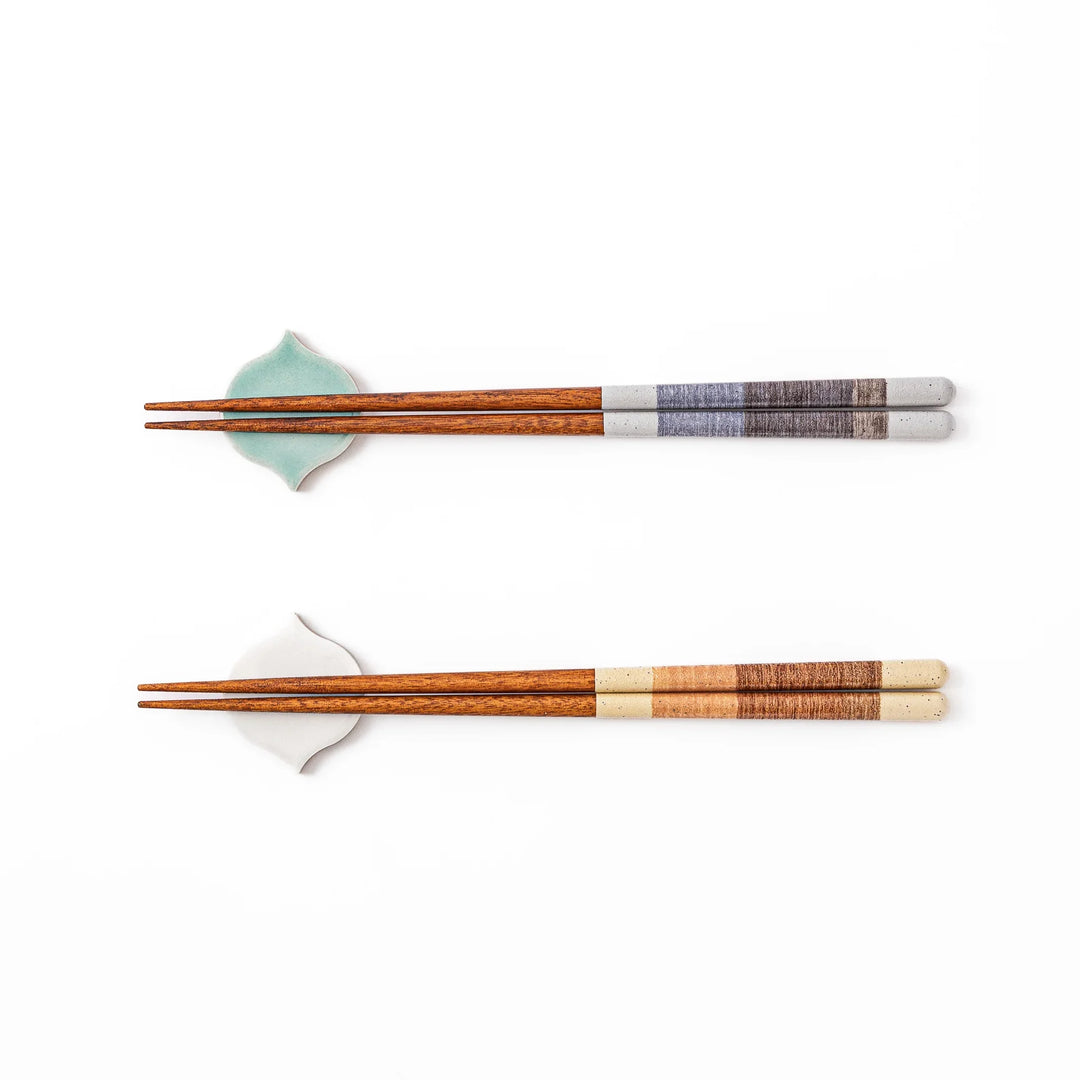Two pairs of natural wood Japanese chopsticks resting on blue and white curved tile style ceramic chopstick rests