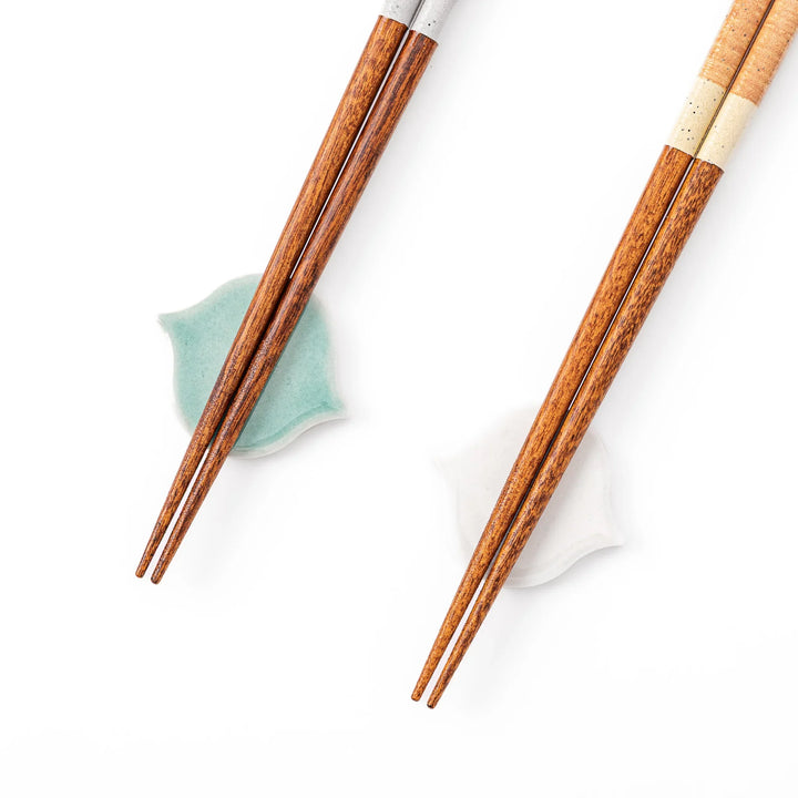 Two pairs of natural wood Japanese chopsticks resting on blue and white curved tile style ceramic chopstick rests