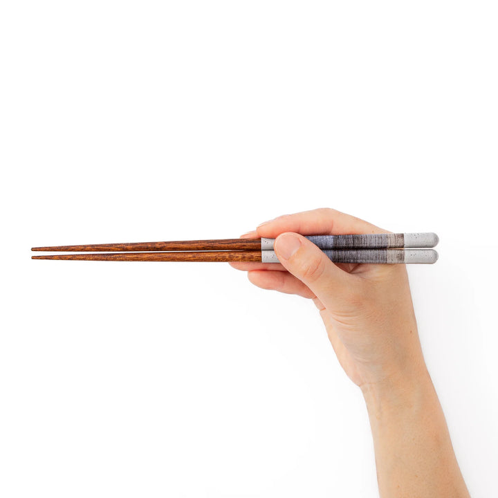 A hand holding a pair of blue gray textured Japanese chopsticks to demonstrate a comfortable natural grip and standard length