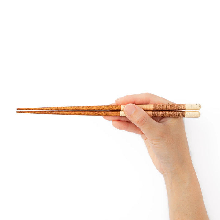 A hand holding a pair of beige textured Japanese chopsticks showcasing the unique earthy tone and minimalist design