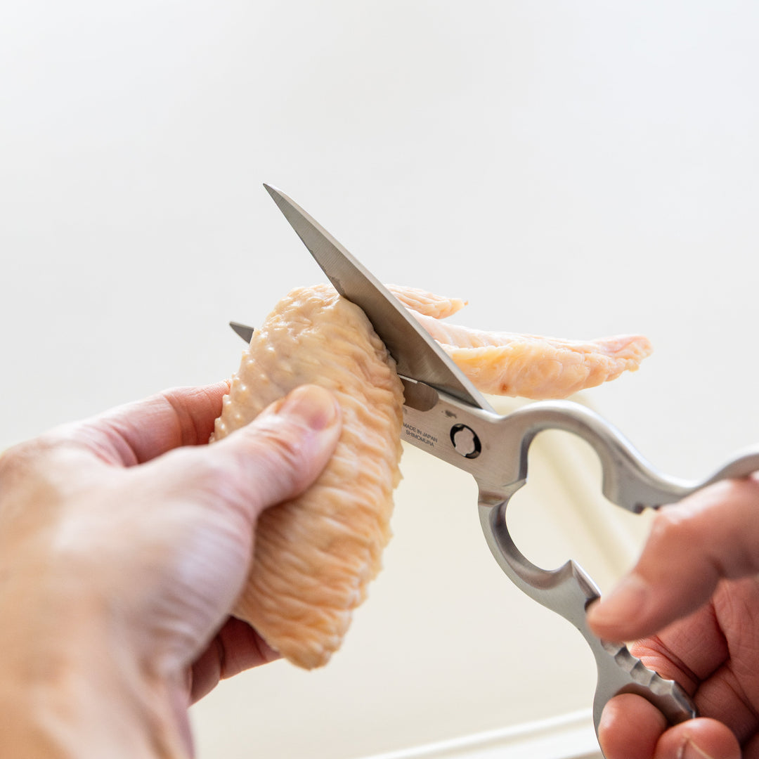 Japanese stainless steel kitchen shears cutting raw chicken wing for meal preparation