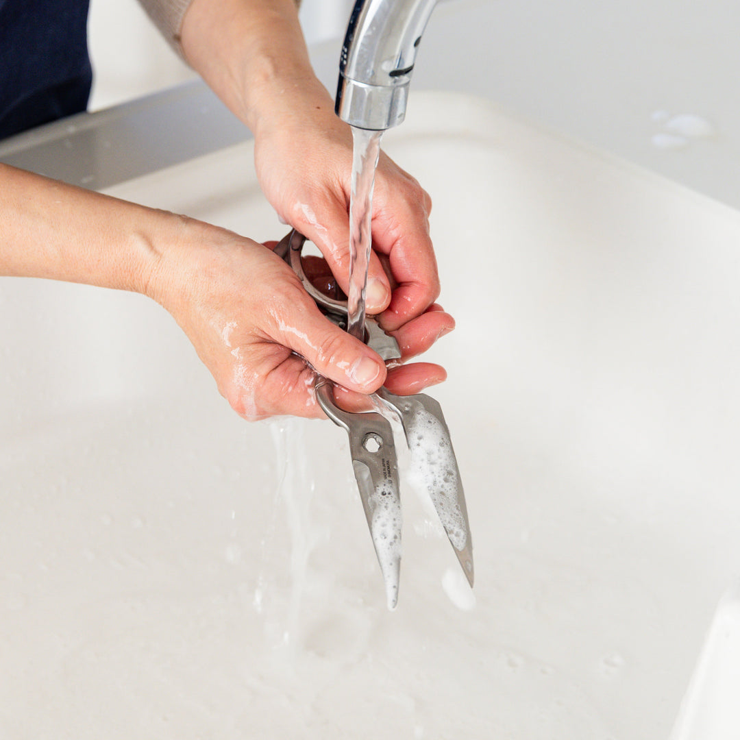 Japanese stainless steel kitchen shears being washed under running water in sink