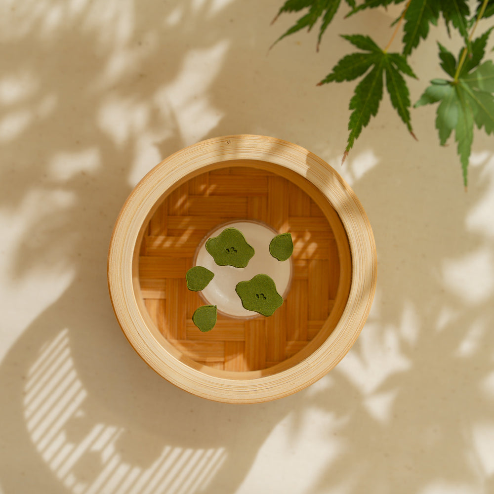 Green Japanese matcha pressed incense shaped like delicate flower petals inside a round bamboo incense warmer