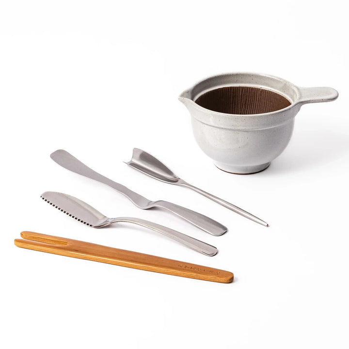 Japanese breakfast utensil set featuring stainless steel butter and fish knives, bamboo tongs, and a ceramic mortar bowl