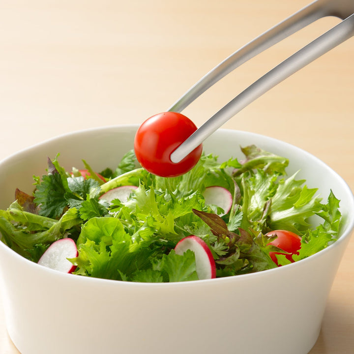 Japanese stainless steel tongs picking up a cherry tomato from a salad bowl to show precision and delicate handling