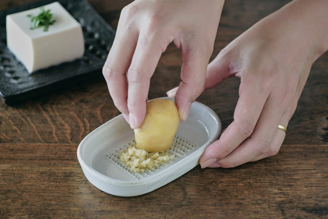 Hand grating fresh ginger on a ceramic ginger grater on a wooden kitchen table