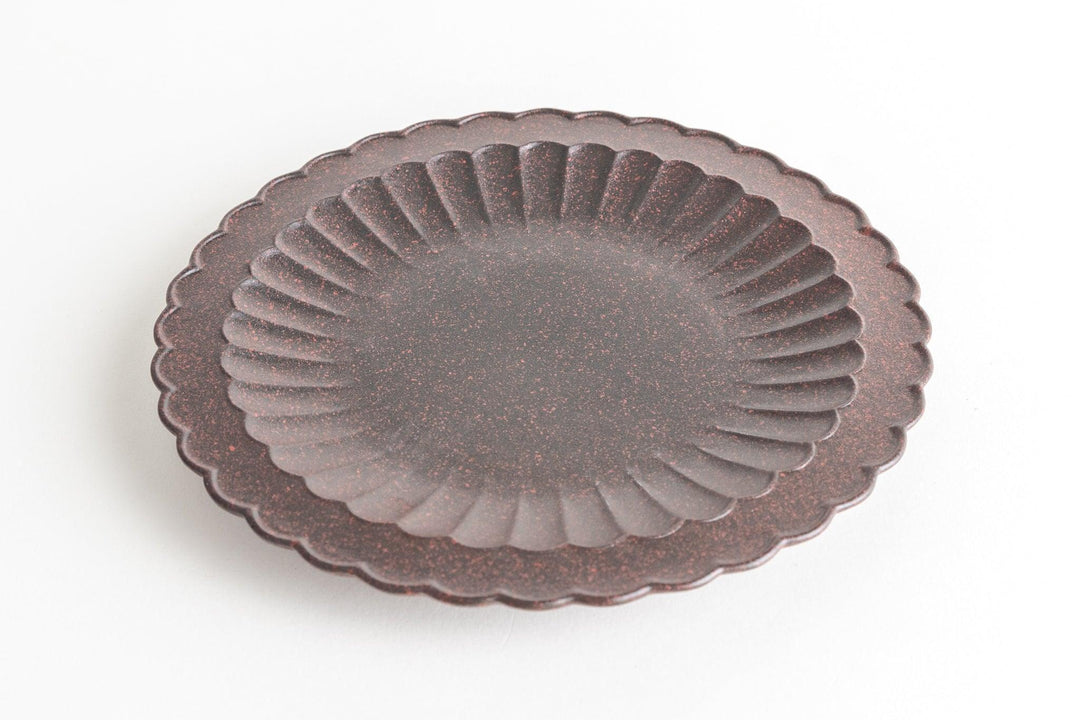 Dark brown ceramic plate with a scalloped rim and radial textured pattern on a light background.