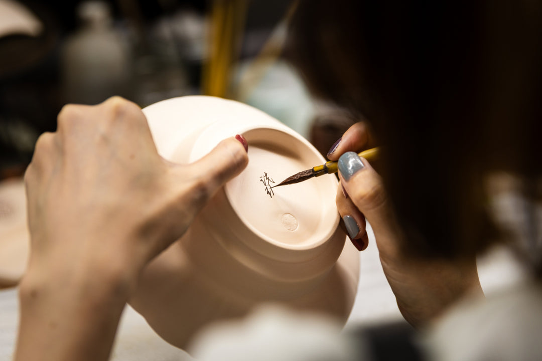 Artisan hand painting the base of a ceramic bowl with a fine brush in a pottery workshop