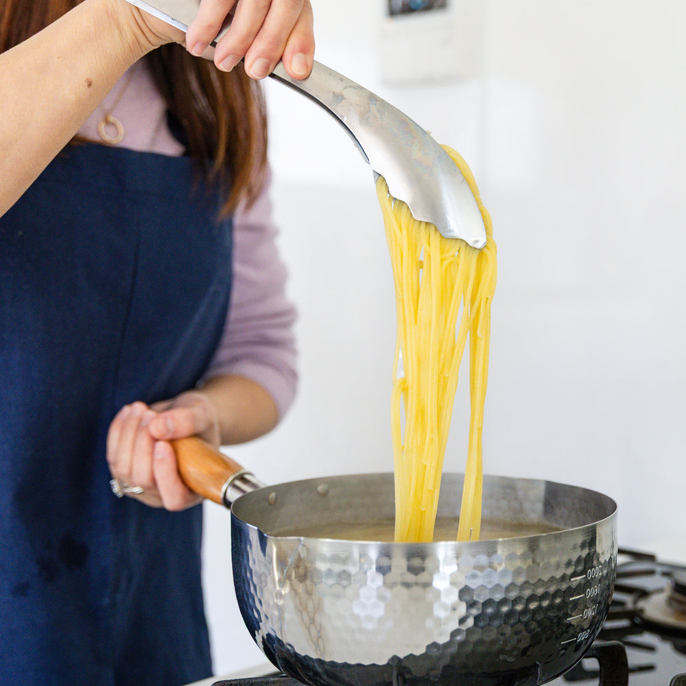 Nami from Just One Cookbook lifting a large serving of noodles with Japanese stainless steel tongs from a boiling pot
