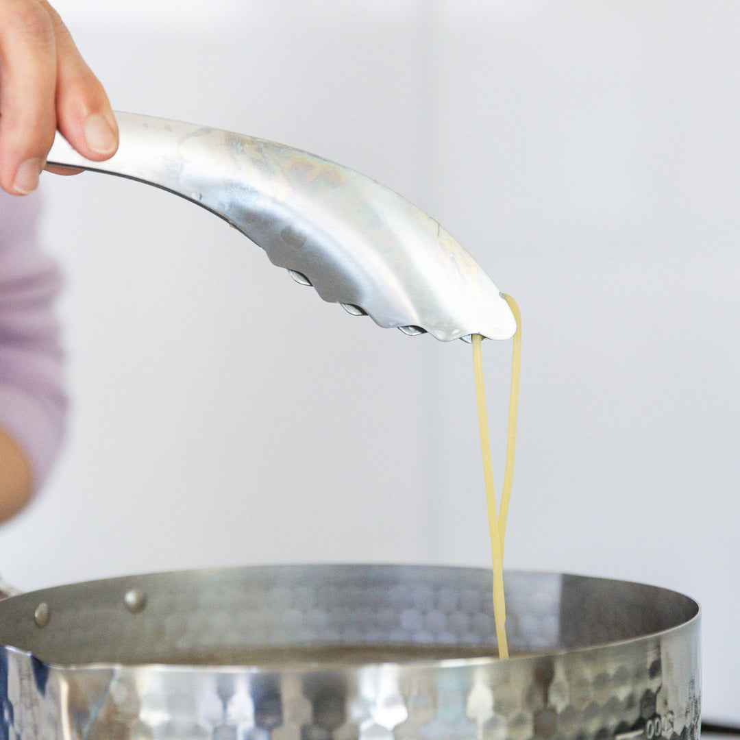 Nami from Just One Cookbook lifting a single strand of pasta with stainless steel tongs to check for doneness