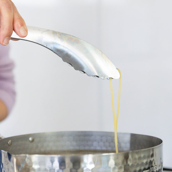 Nami from Just One Cookbook lifting a single strand of pasta with stainless steel tongs to check for doneness