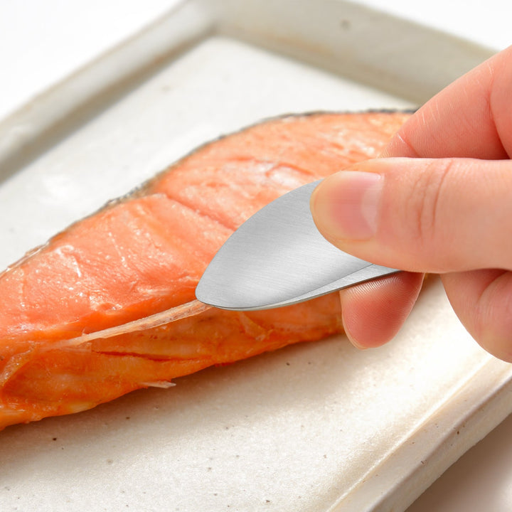 Small stainless steel tongs pulling a bone from a grilled salmon fillet to demonstrate a firm and accurate grip