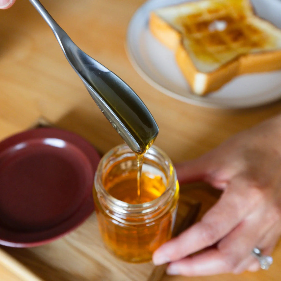 Nami lifting aux japanese honey spoon filled with golden organic syrup over glass jar breakfast buttered toast