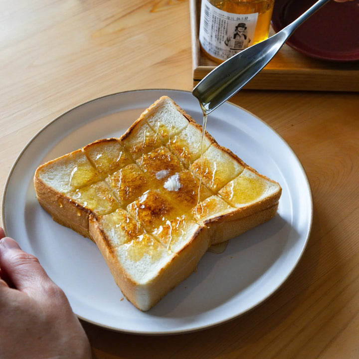 Nami drizzling sweet syrup using aux japanese honey spoon onto crispy hot buttered toast on ceramic dinner plate