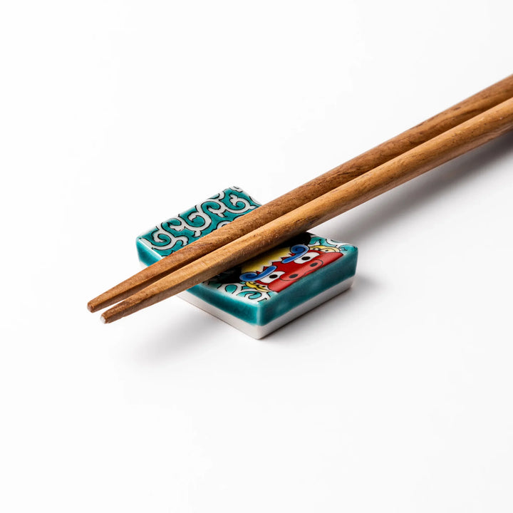 Rectangular Japanese ceramic chopstick rest with red lion dance motif and green swirl background for dining.