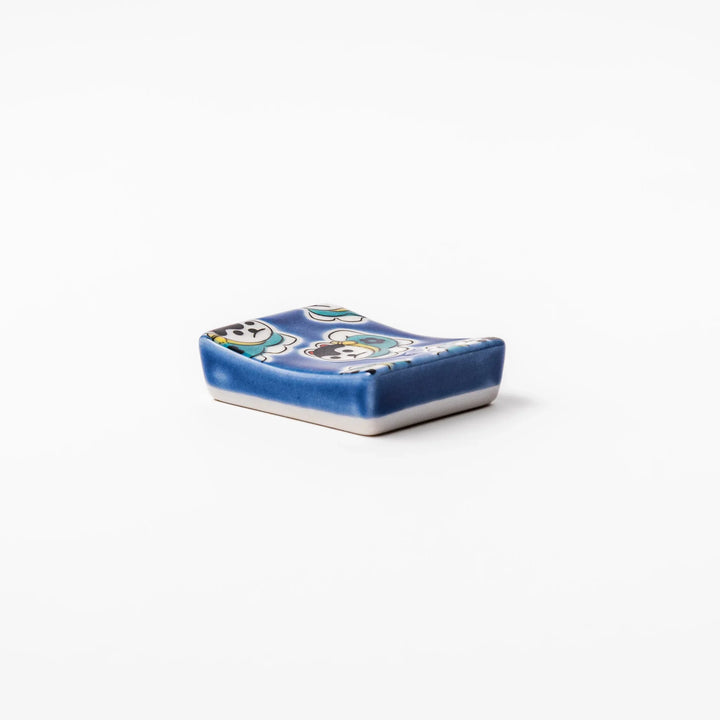Rectangular Japanese ceramic chopstick rest with deep blue background and playful lucky dog motifs.