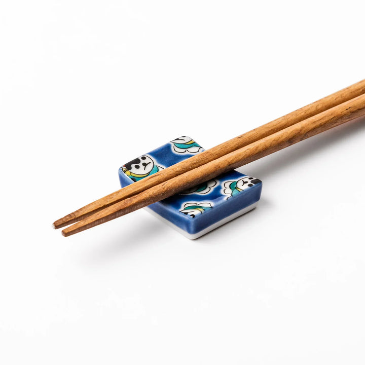 Rectangular Japanese ceramic chopstick rest with deep blue background and playful lucky dog motifs.