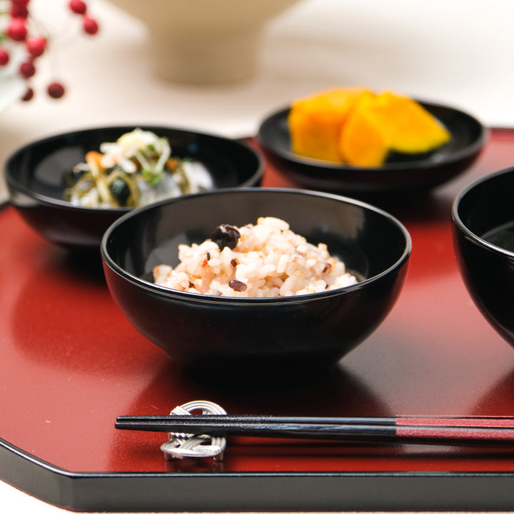 Black lacquer rice bowl on a red Japanese tray with mixed grain rice and seasonal side dishes