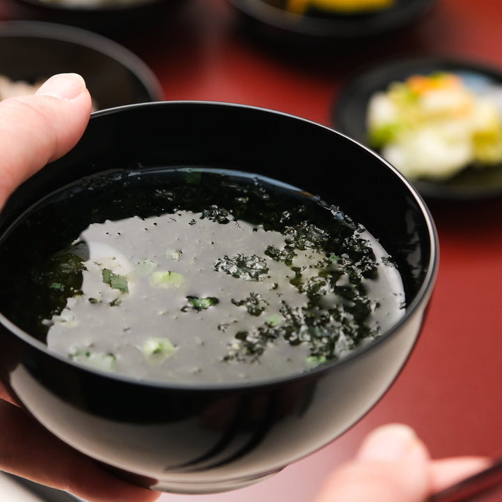 Black lacquer soup bowl held in hand with clear Japanese seaweed soup