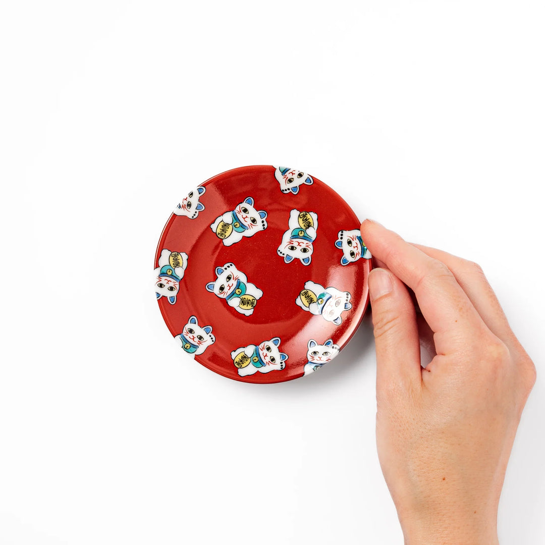 Round Japanese ceramic sauce dish with red background and maneki neko cat design for soy sauce or condiments.