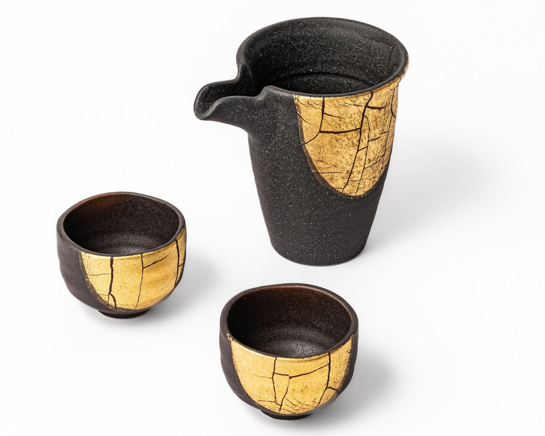 Kintsugi inspired black Kutani sake set with gold accents including a serving carafe and two matching cups on white background