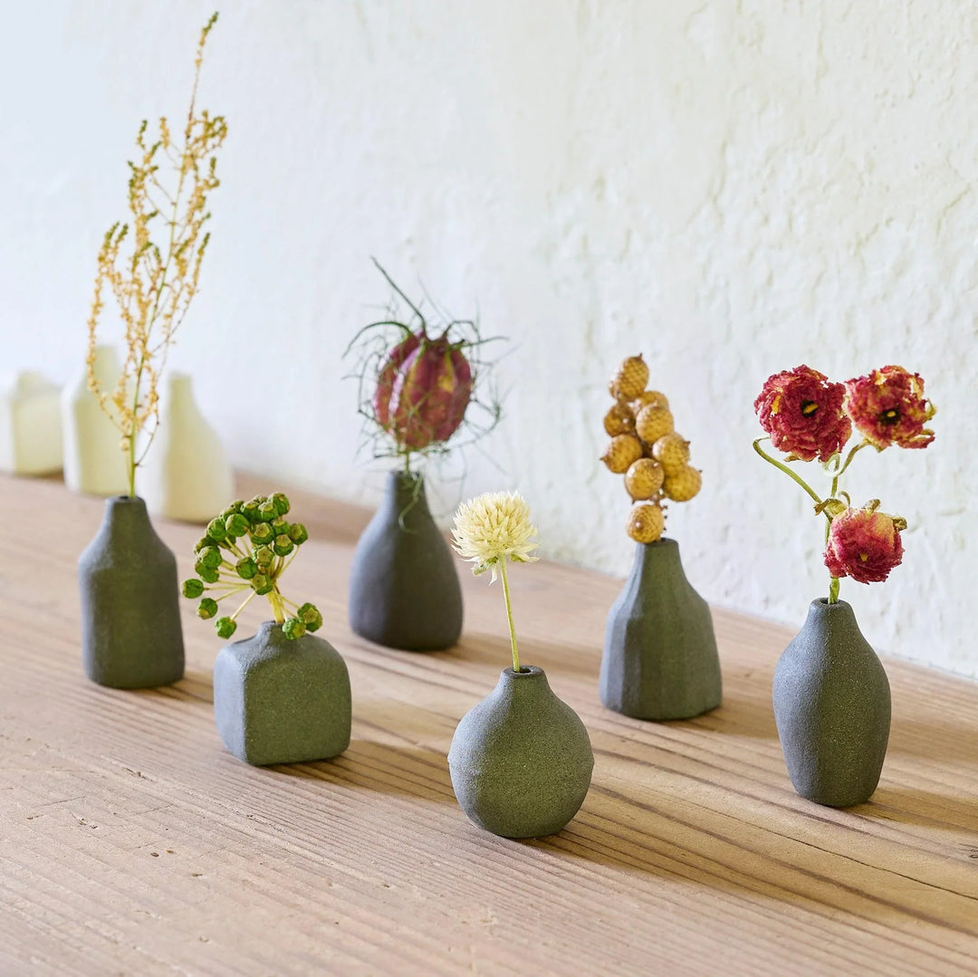 Black minimalist ceramic bud vases in geometric shapes on wooden table displaying dried wildflowers for home decor