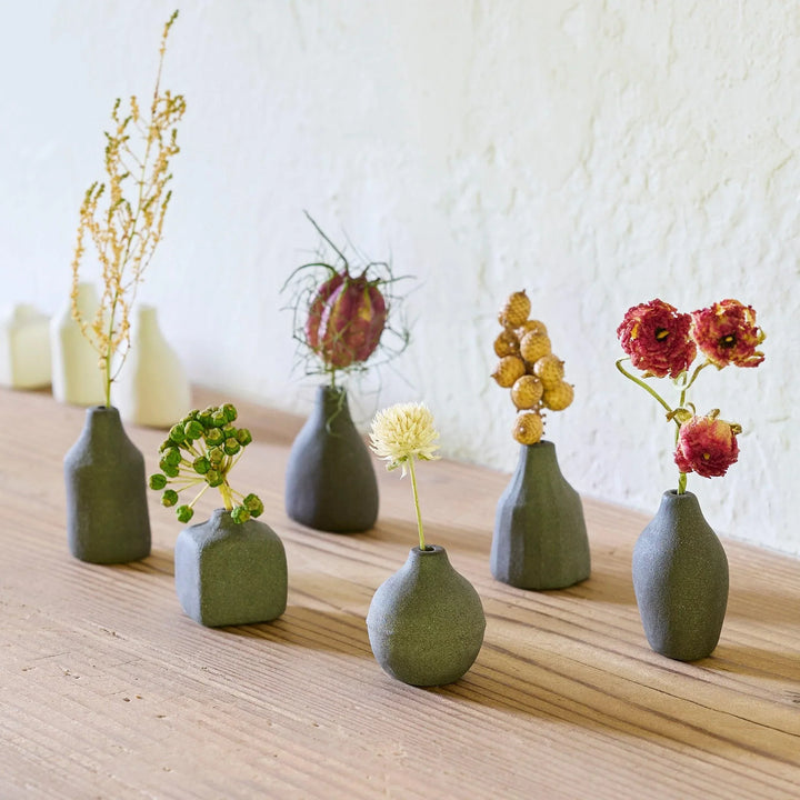 Black minimalist ceramic bud vases in geometric shapes on wooden table displaying dried wildflowers for home decor