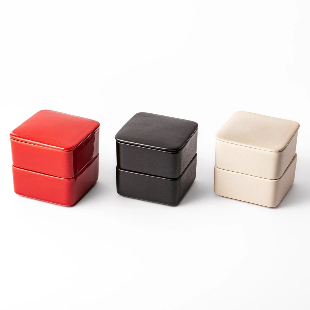 Modern Japanese ceramic bento boxes in red, black, and ivory, stackable two-tier design for elegant meal presentation.