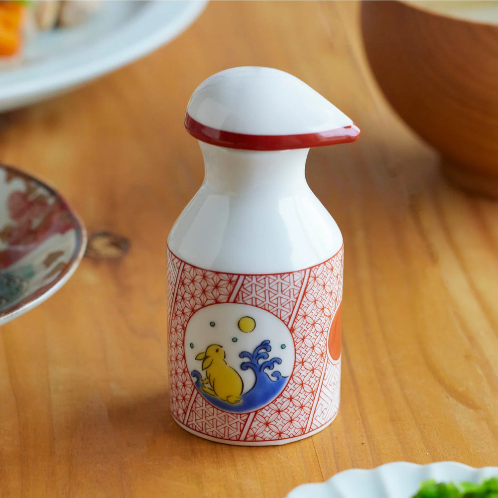 Porcelain soy sauce dispenser with red geometric patterns and a moon rabbit motif, placed on a wooden dining table.