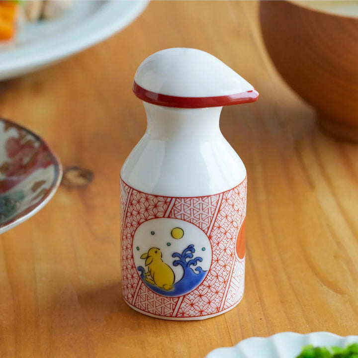 Porcelain soy sauce dispenser with red geometric patterns and a moon rabbit motif, placed on a wooden dining table.