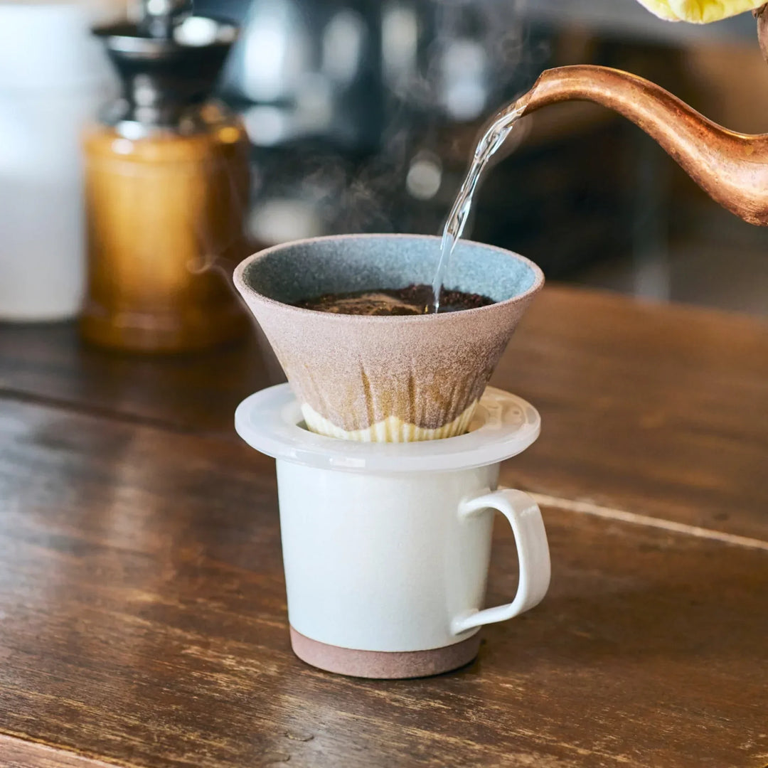 Handcrafted ceramic coffee filter shaped like Mount Fuji in warm cocoa brown, brewing aromatic pour over coffee in a calm kitchen.