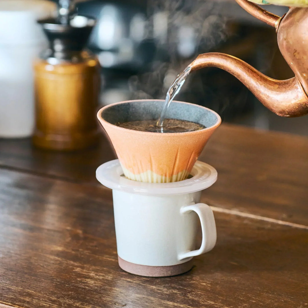 Handcrafted ceramic coffee filter inspired by Mount Fuji in soft orange glaze, pouring freshly brewed coffee for a warm and peaceful morning.