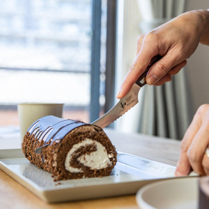 Nagomi Japanese cake knife with a serrated stainless steel blade smoothly slicing through a chocolate rolled cake