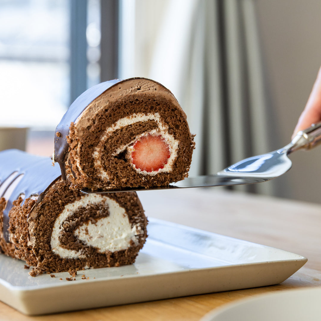 Nagomi stainless steel cake server lifting a slice of chocolate rolled cake with a whole strawberry inside