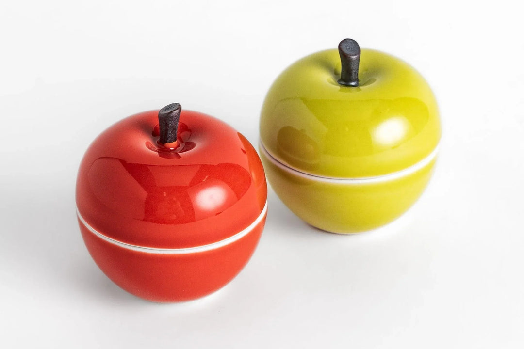 Glossy apple shaped containers in red and green with dark stems, designed for playful kitchen or table storage.