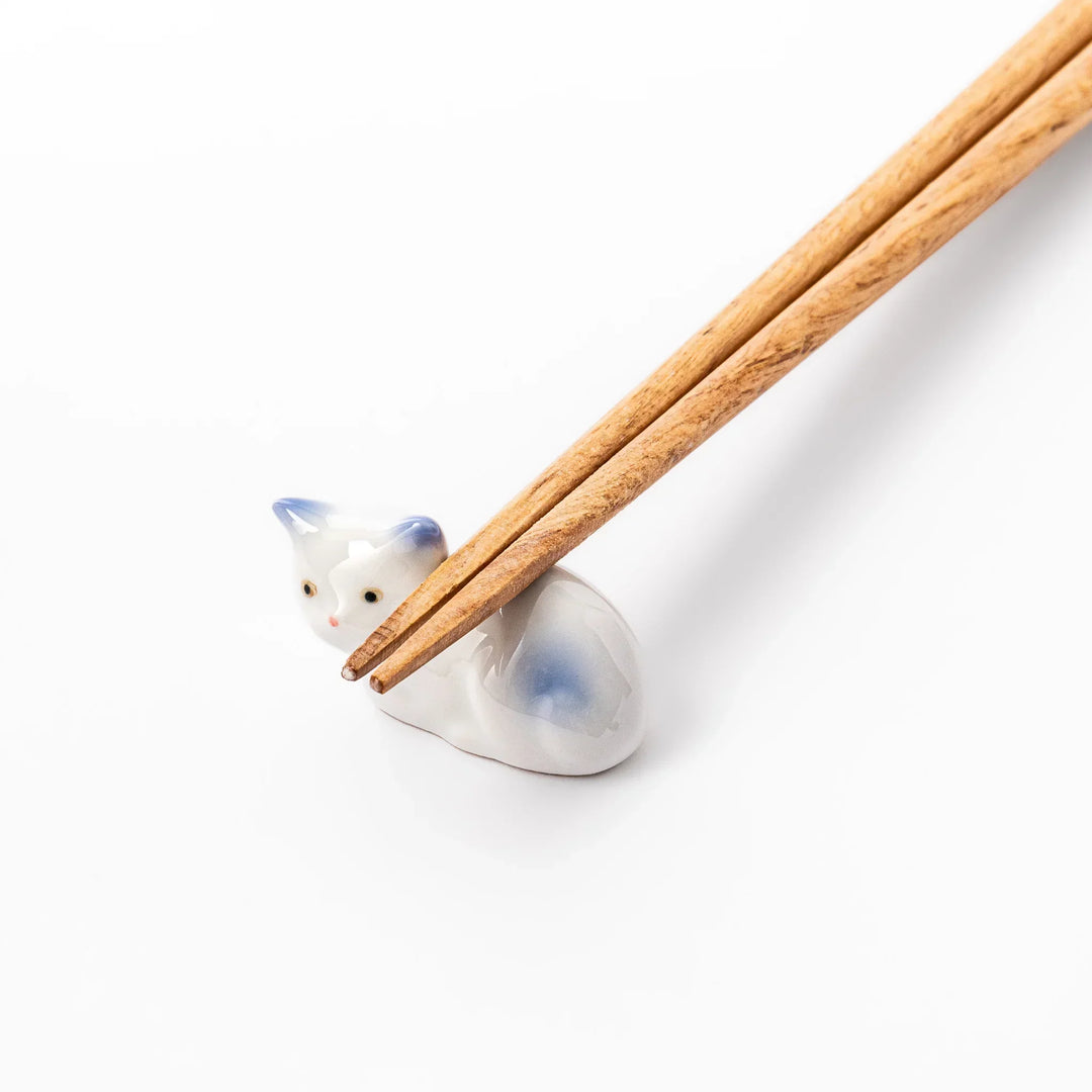 White ceramic chopstick rest shaped like a reclining cat with soft blue accents and a glossy finish.