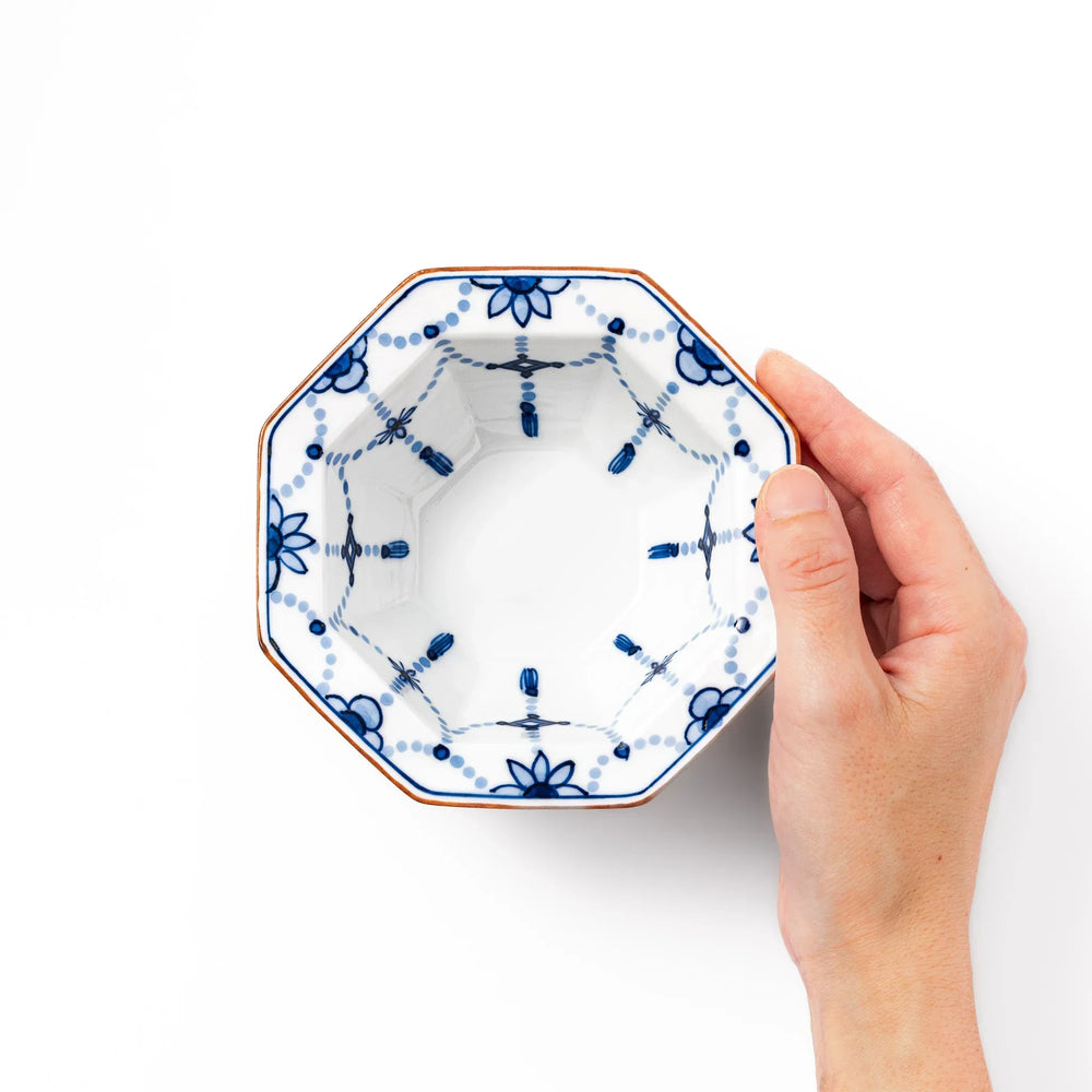 White octagonal dessert bowl with blue floral garland and red rim featuring fine geometric detailing.