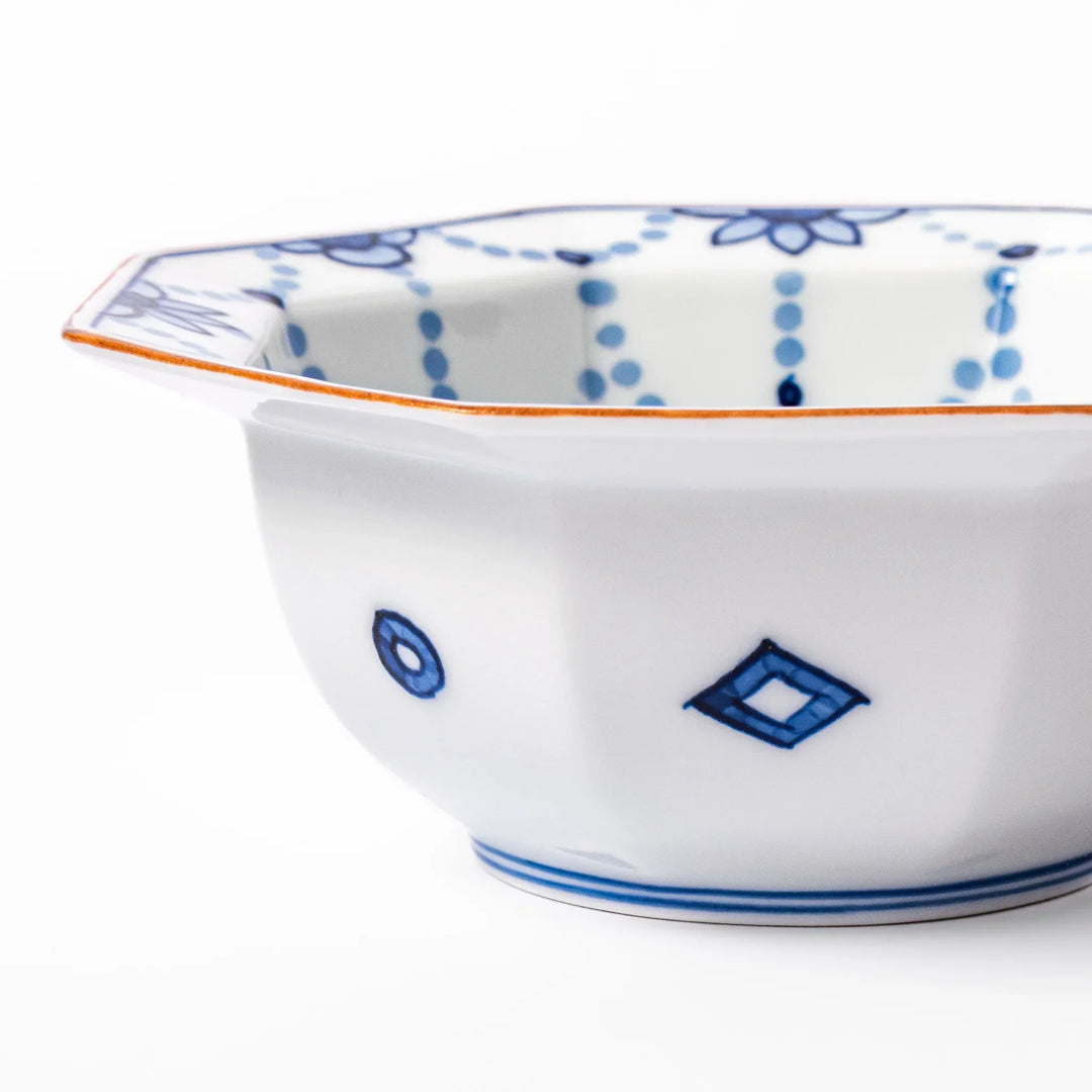 White octagonal dessert bowl with blue floral garland and red rim featuring fine geometric detailing.