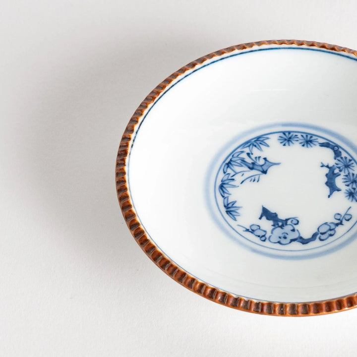 Small ceramic plate with central blue floral motif on white background framed by copper textured rim.