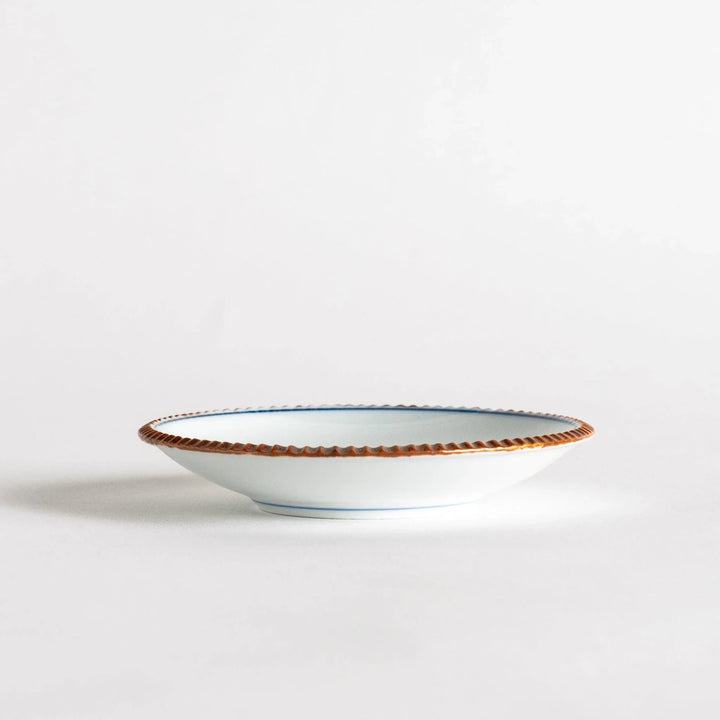 Small ceramic plate with central blue floral motif on white background framed by copper textured rim.
